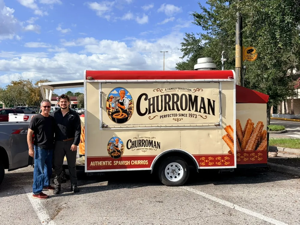 Jacob Castillo y Eliu Castillo sonriendo junto al puesto de Churroman de hoy en West Waters Avenue