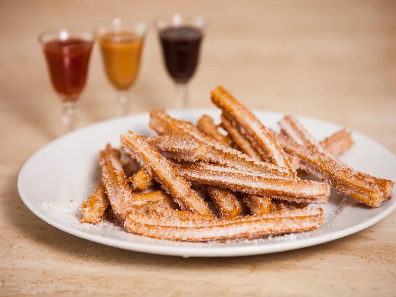 A plate of sugar-dusted churros with guava, dulce de leche and chocolate dipping sauces